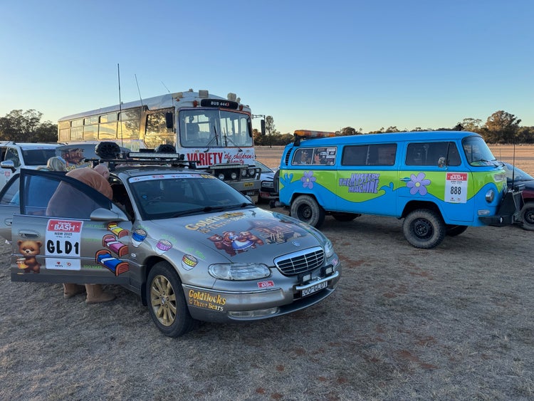 Three vehicles in the variety bash: The big variety Bus, a light blue combi van and a gold sedan.